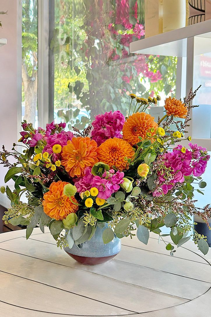 a vase filled with lots of different colored flowers on top of a table next to a window