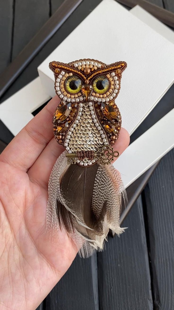 a hand holding an owl brooch with feathers on it's back and eyes