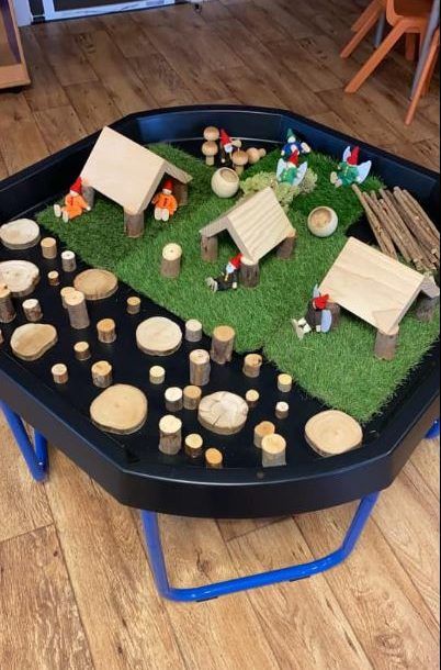 a table that has some little houses on top of it and grass in the middle