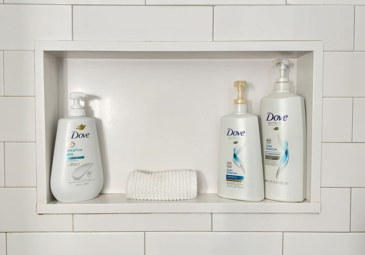 two bottles of hand soap and lotion sitting on a shelf in a white tiled bathroom