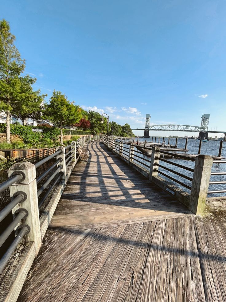 a wooden pier with benches and railings next to the water on a sunny day