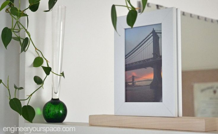 a green vase sitting on top of a white shelf next to a framed photo and a plant