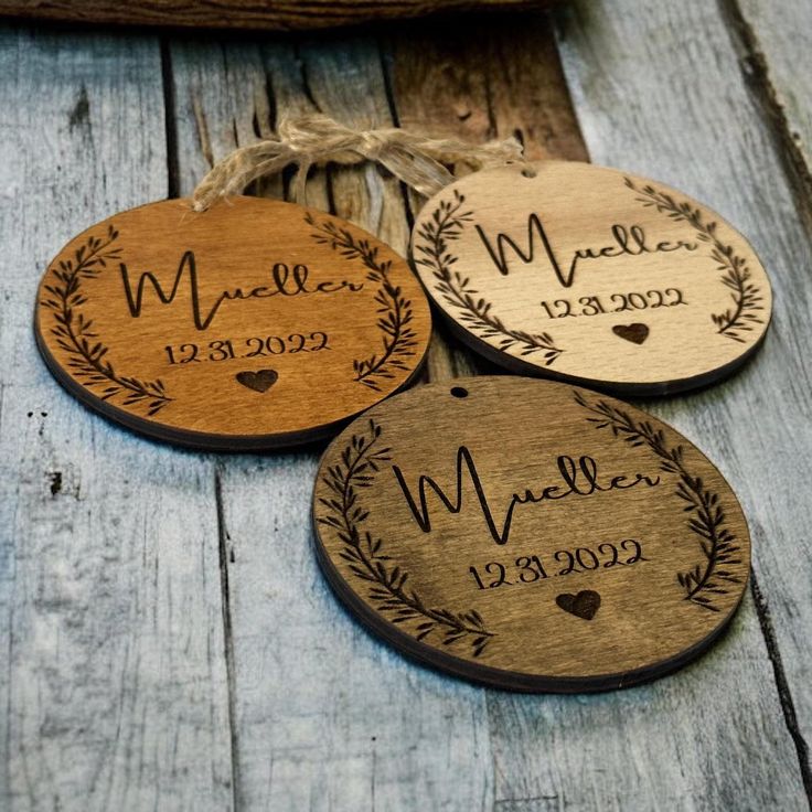 three personalized wooden ornaments with names and date printed on the front, hanging from twine strings