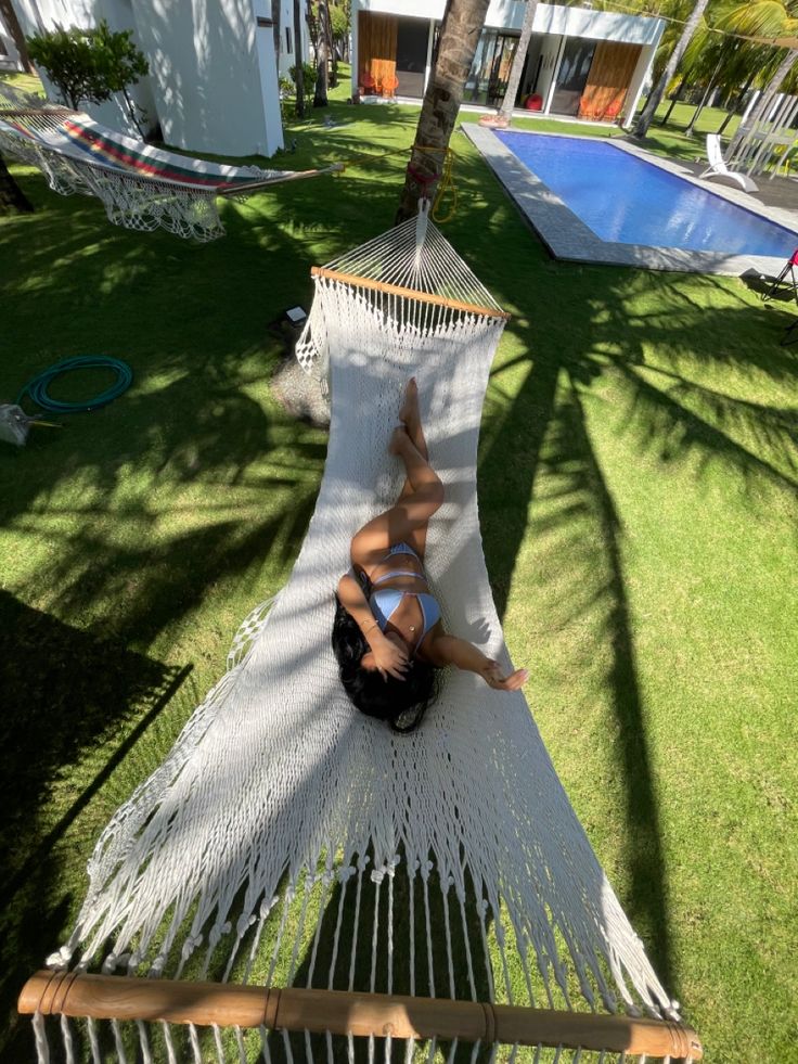 a woman laying in a hammock with her feet on the ground next to a swimming pool