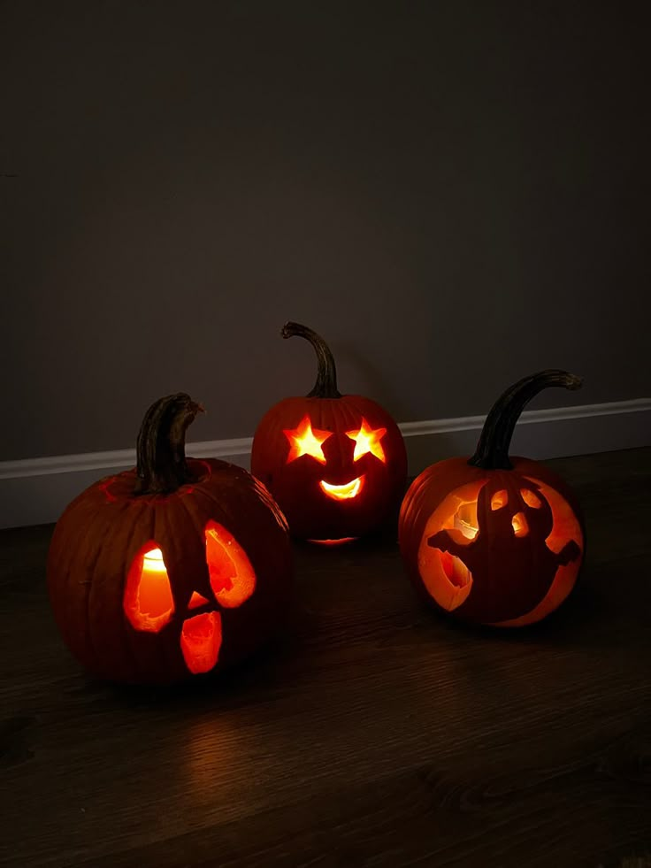 three carved pumpkins sitting on top of a wooden floor