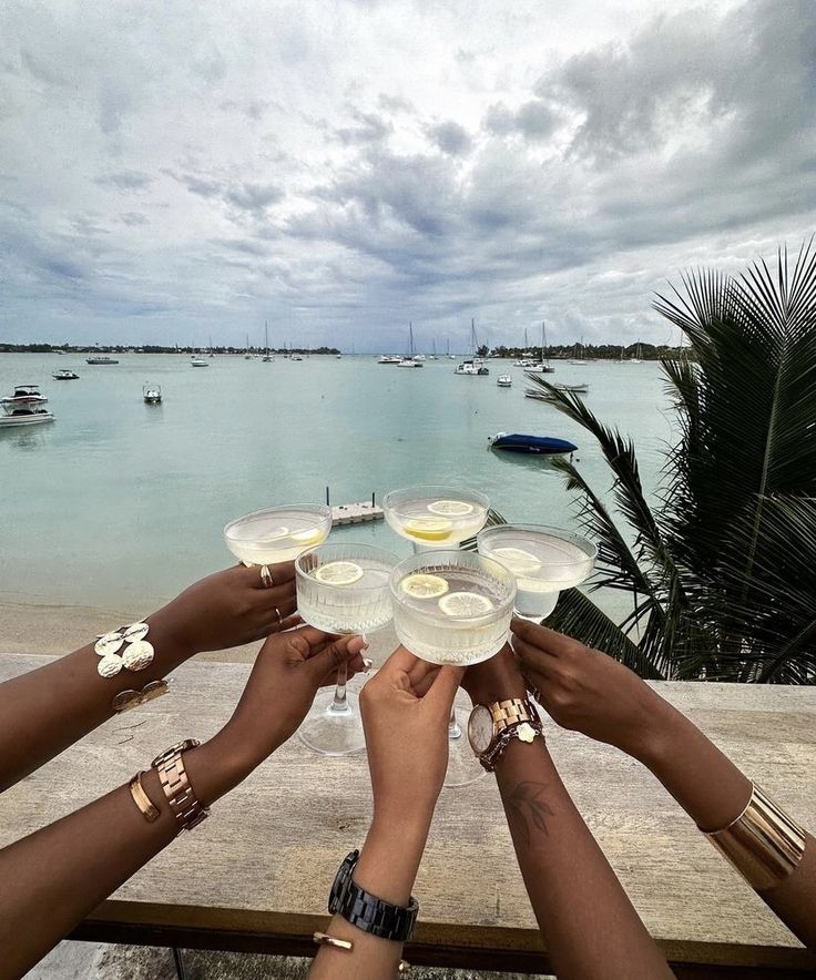 several people are holding wine glasses in front of the ocean with boats on the water