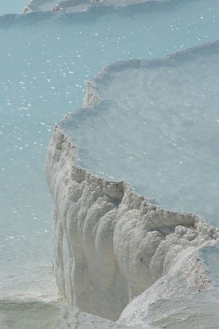 a man standing on the edge of a cliff in front of blue water and ice