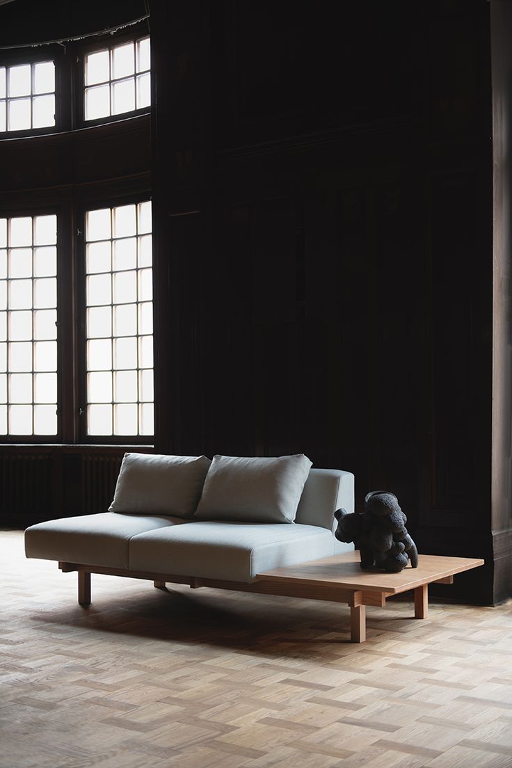 a white couch sitting on top of a wooden floor next to two windows in a dark room