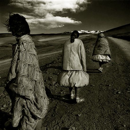 three women walking down a dirt road under a cloudy sky