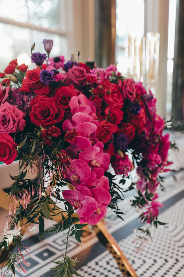 a bouquet of red and pink flowers on a table with other flowers in the background