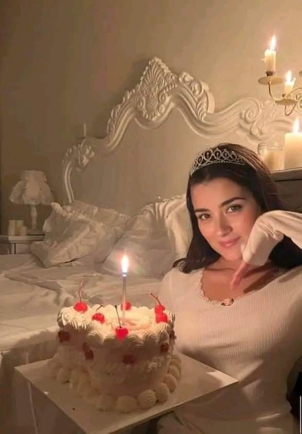 a woman sitting in front of a cake with lit candles on it and posing for the camera