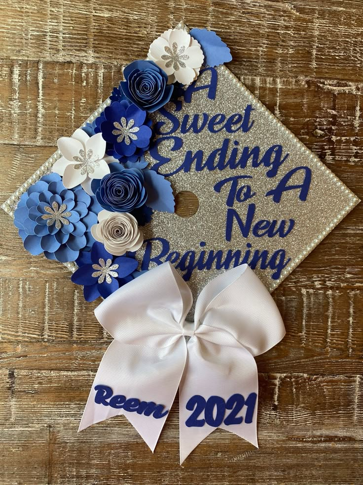 a blue and white graduation cap with flowers on the side, next to a ribbon