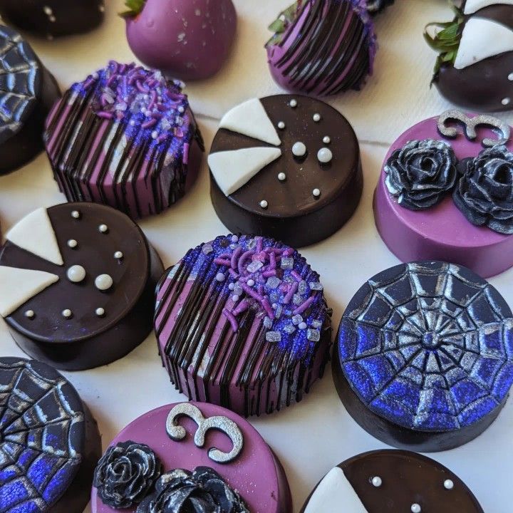 many decorated chocolates are arranged on a table with purple and black frosted decorations