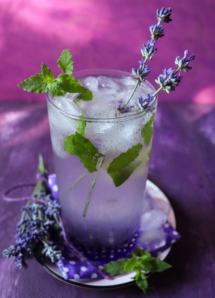 a glass filled with ice and lavender sprigs on top of a purple plate