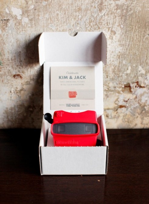 a red toy car in a white box on a wooden table next to a wall