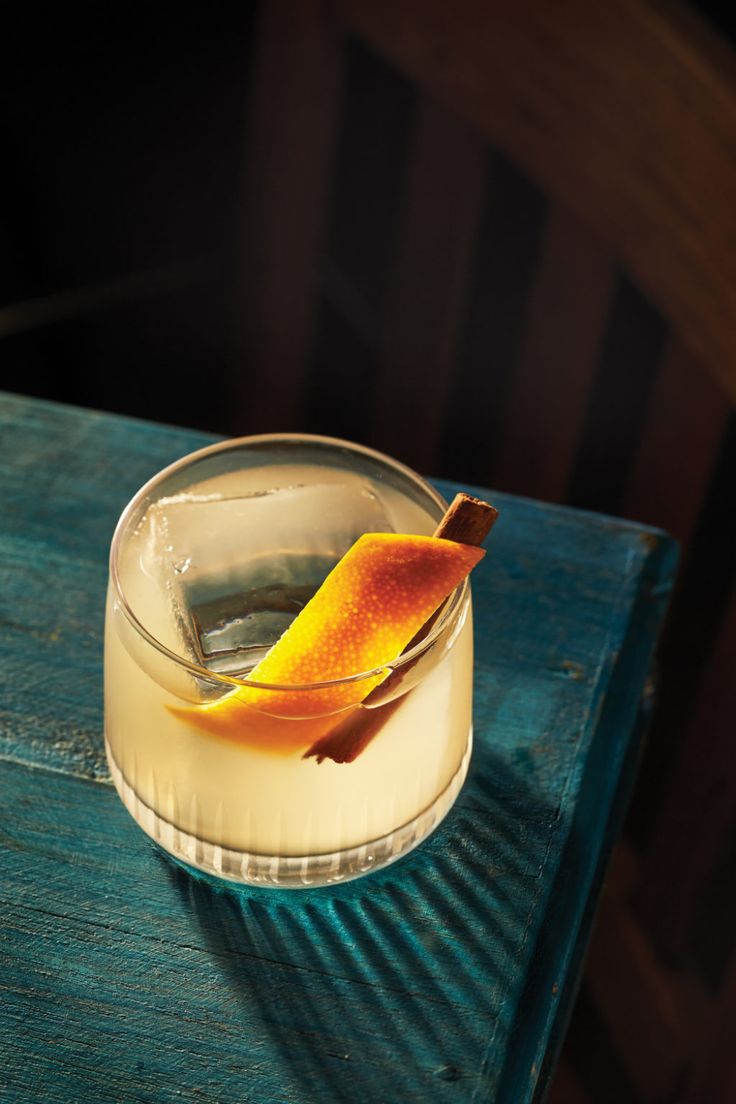 an orange peel is sitting in a glass on a blue wooden table with a green surface