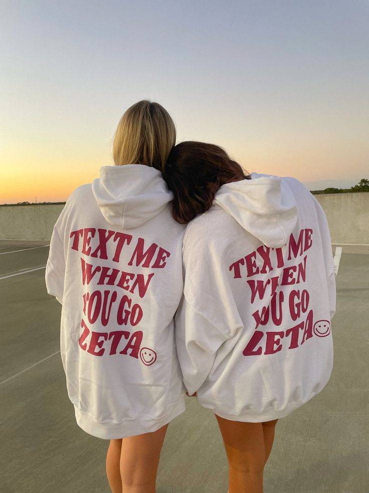 two women in white sweatshirts with texting on them, back to the camera