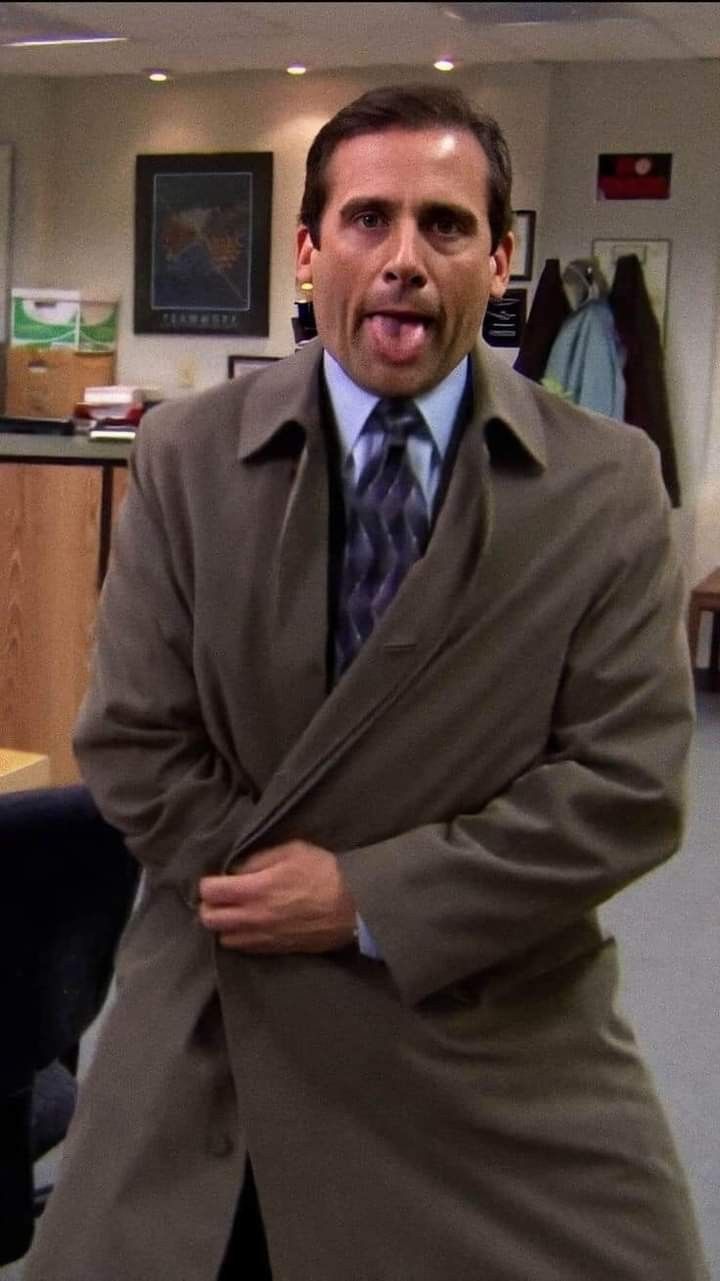 a man in a coat and tie making a funny face while standing in an office