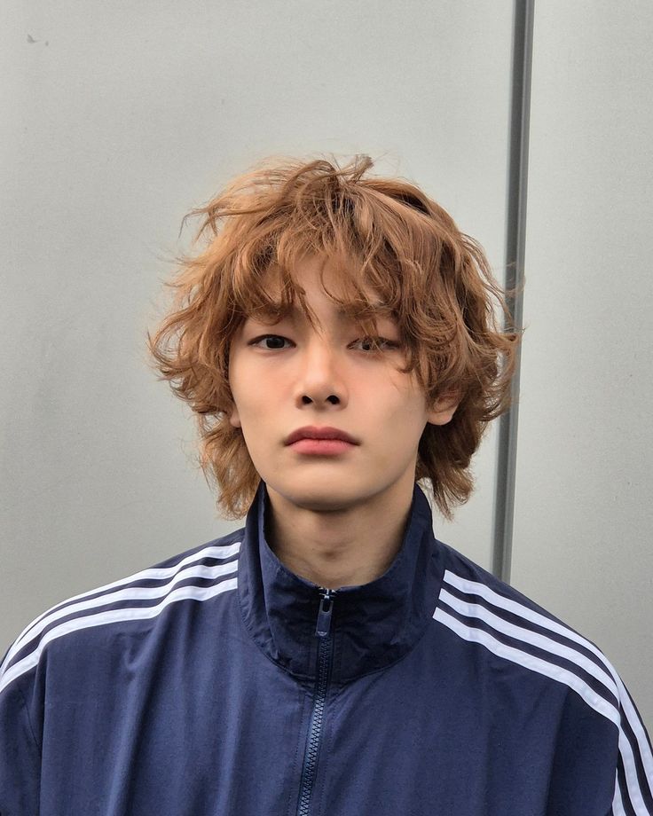 a young man with curly hair wearing a blue jacket