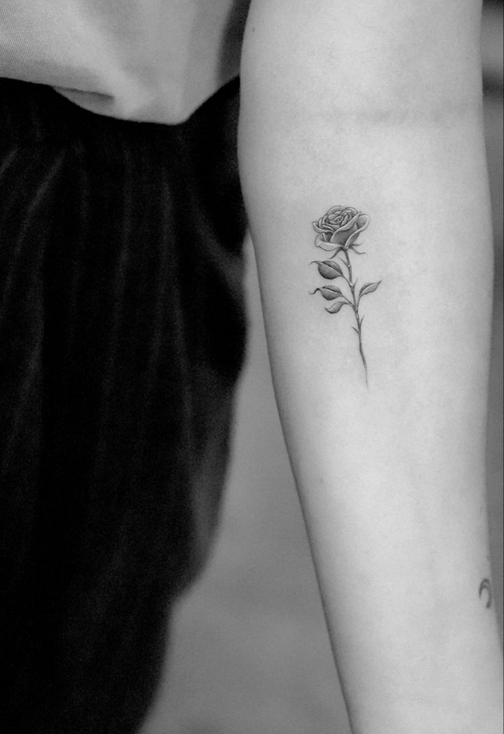 a black and white photo of a woman's arm with a rose tattoo on it