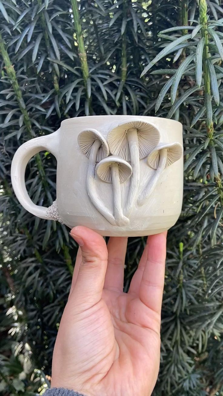 a hand holding a ceramic mug with two mushrooms on it