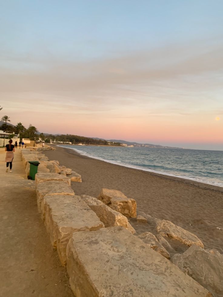 people walking on the beach at sunset with large rocks in foreground and ocean in background