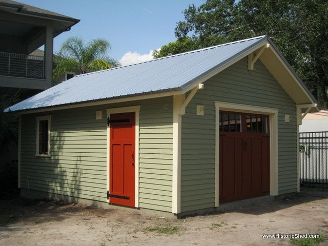 a small garage with a red door in front of a fenced in backyard area