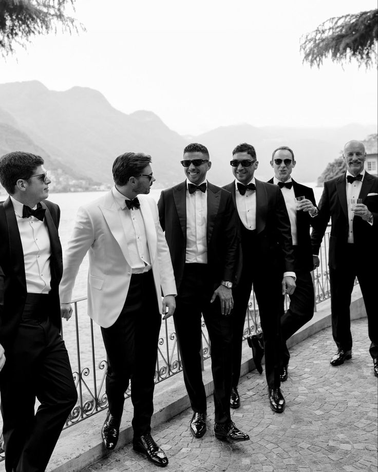 a group of men in tuxedos standing next to each other near the water