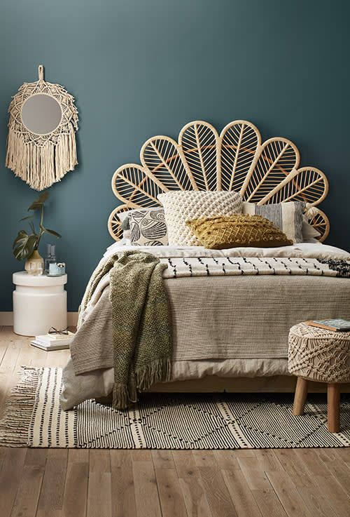 a bedroom with blue walls and wooden flooring has a rattan headboard on the bed