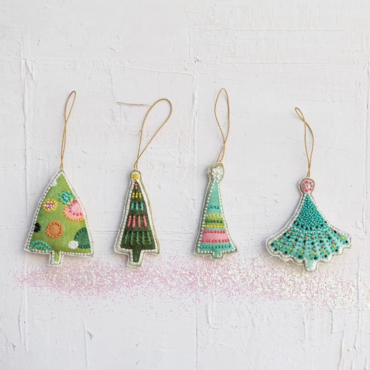 three christmas trees hanging from strings on a white wall with pink and green sprinkles