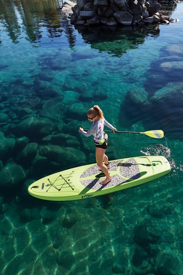 a woman is standing on a surfboard in the clear blue water near some rocks