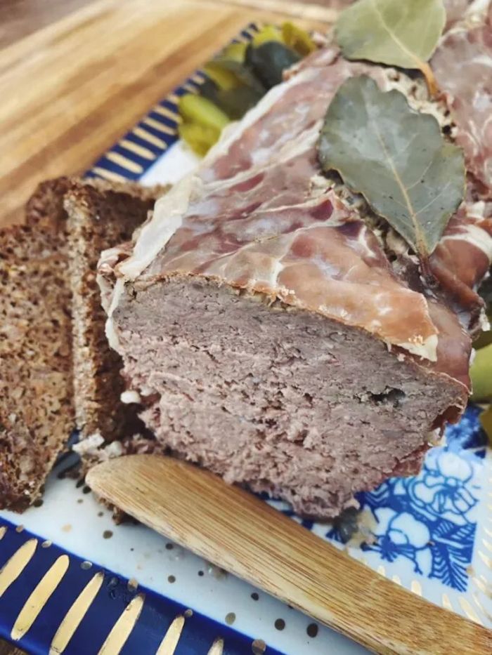 sliced meatloaf on a blue and white platter with bread, grapes, and green beans