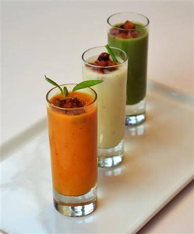 three glasses filled with different types of drinks on a white tray, one is orange and the other is green