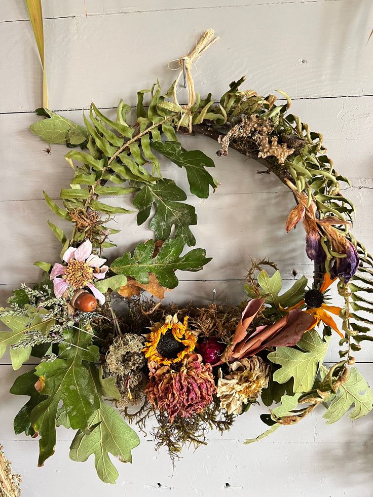 a wreath made out of dried flowers and leaves on a white wooden wall with hanging hooks