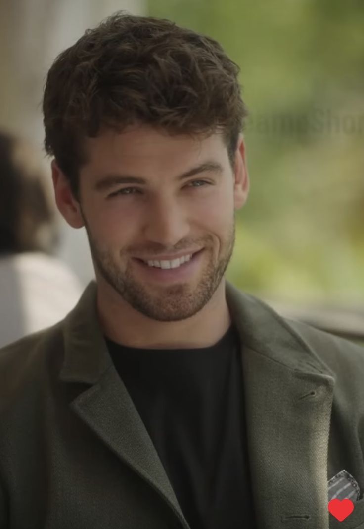 a smiling man in a green jacket and black t - shirt is looking at the camera