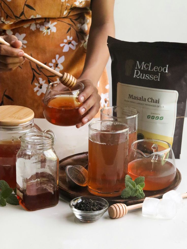 a woman is holding a spoon over some tea and other ingredients on a tray with honey