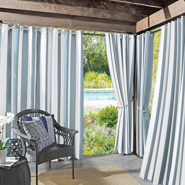 a chair sitting in front of a window covered in blue and white striped drapes