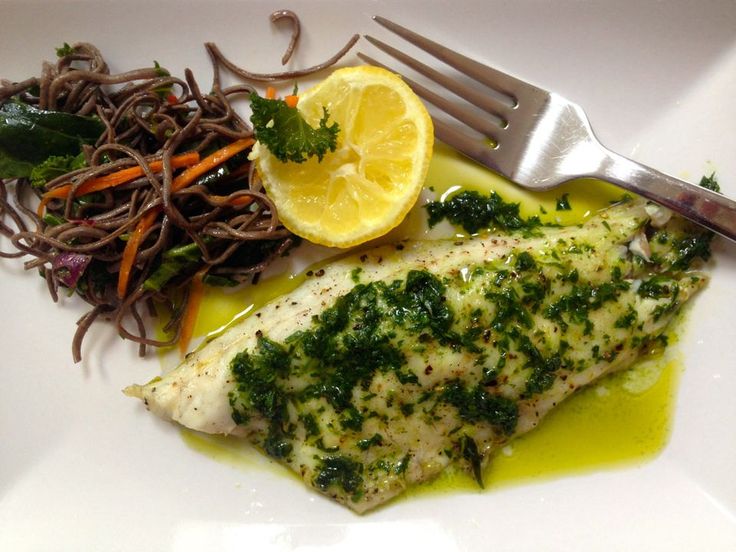 a white plate topped with fish and veggies next to a fork on a table