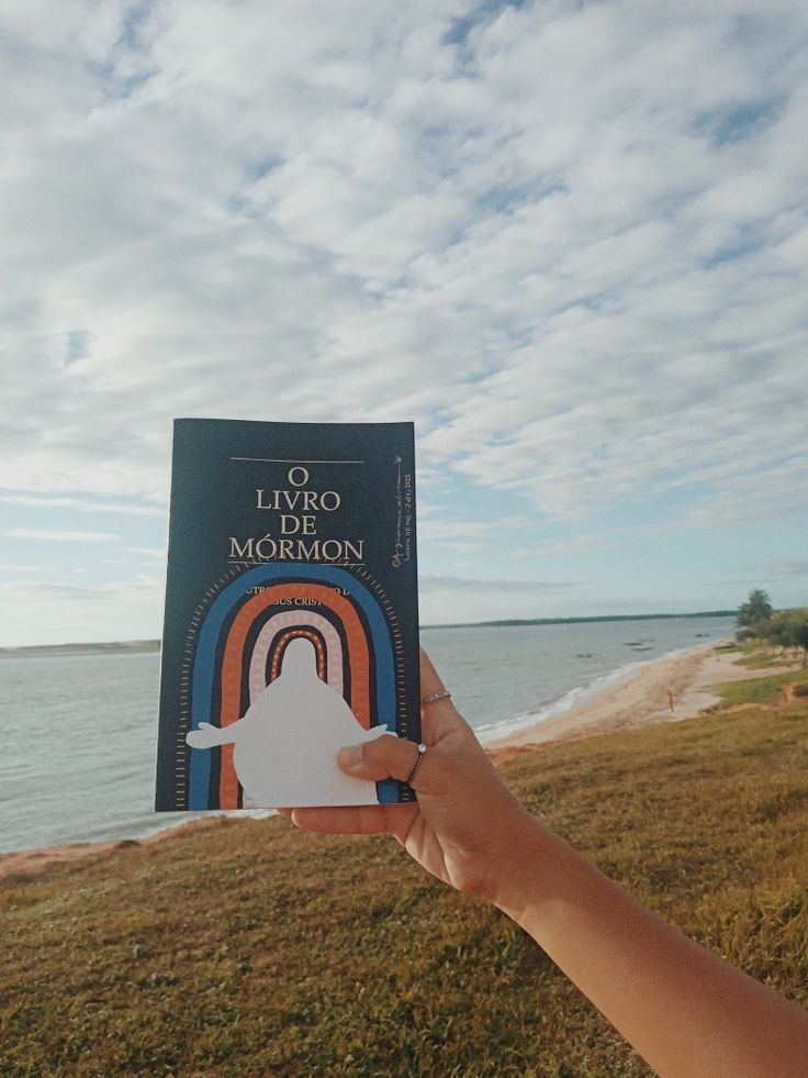 a person holding up a book in front of the ocean