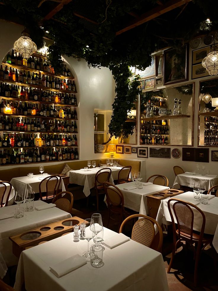 a dimly lit dining room with many bottles on the wall and tables set for four