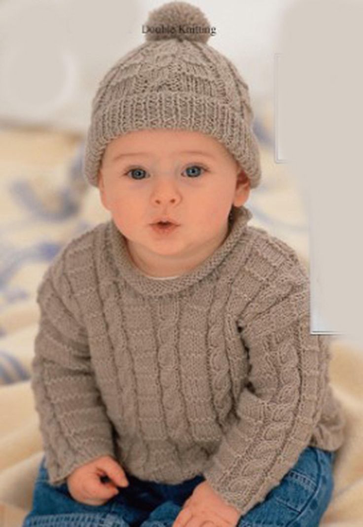 a baby sitting on top of a bed wearing a knitted hat