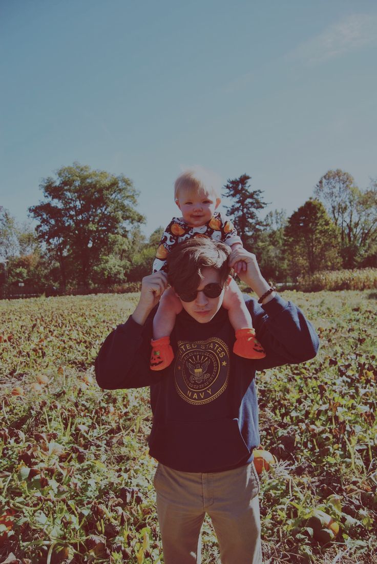 a man holding a baby on his shoulders while standing in the middle of a field