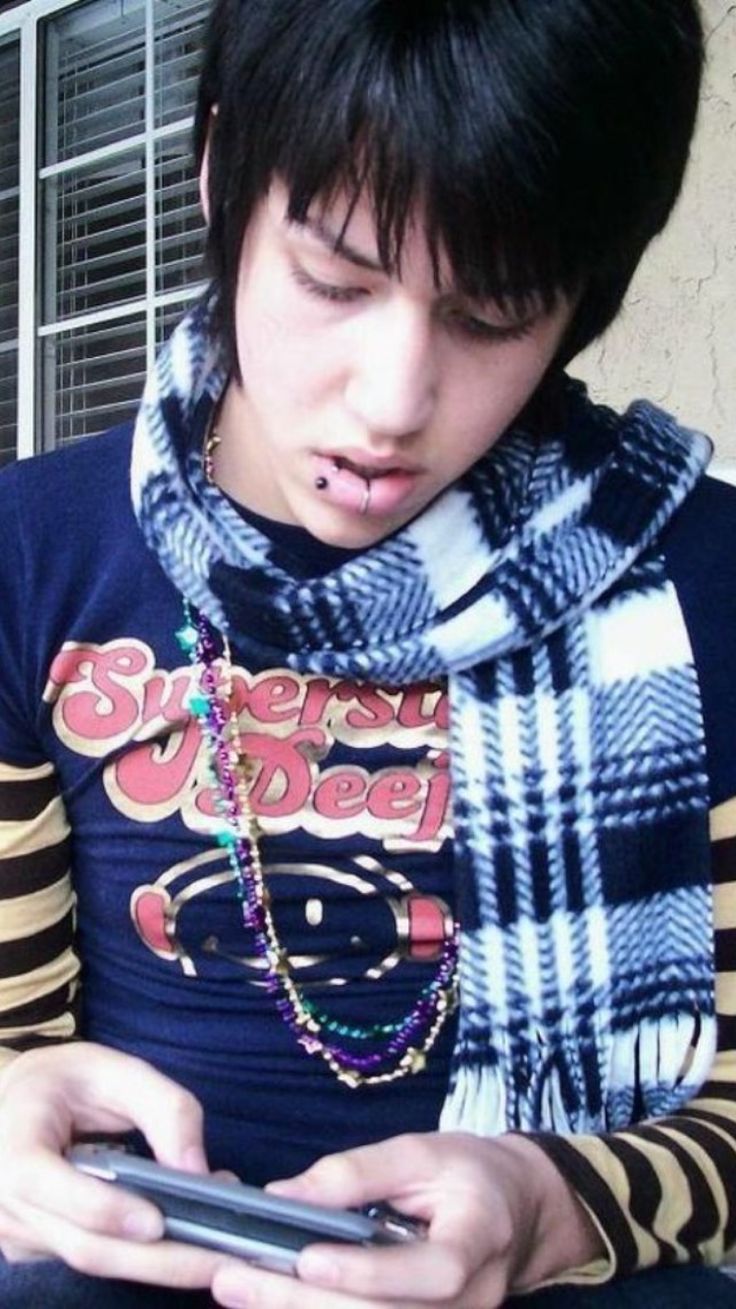 a young man looking at his cellphone while wearing a scarf around his neck and striped shirt