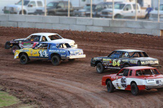 three dirt racing cars driving on a track in the dirt with other cars behind them