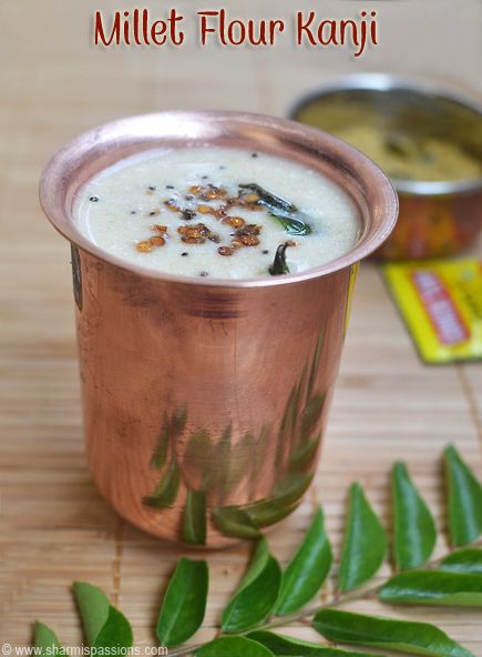 a copper cup filled with food on top of a wooden table next to green leaves