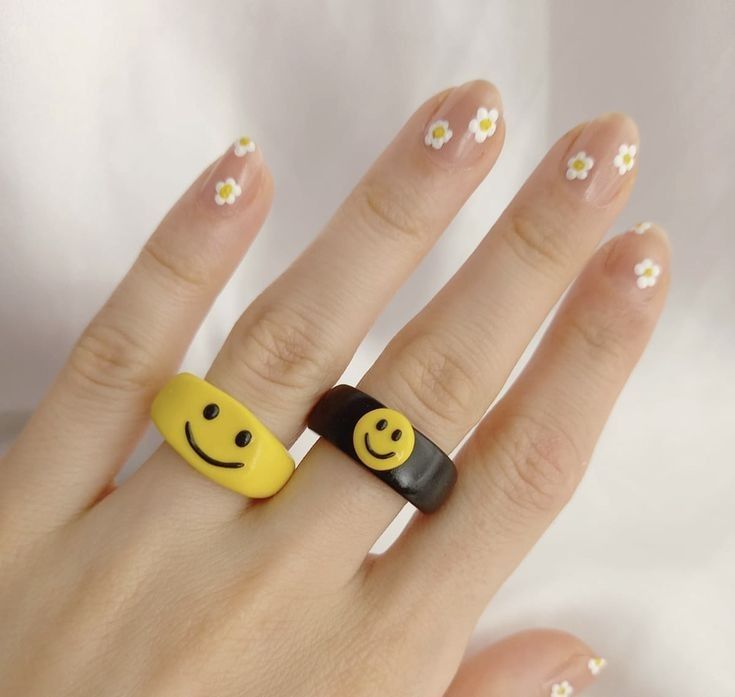 a woman's hand with yellow and black smiley face rings on it, while the fingers are decorated with daisies