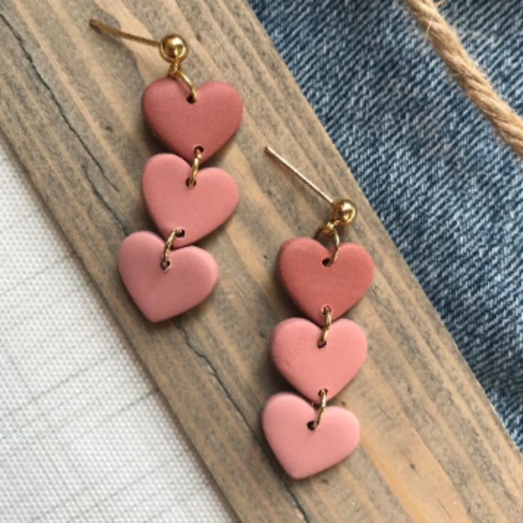 three heart shaped pink and gold earrings on top of a piece of wood next to a pair of jeans