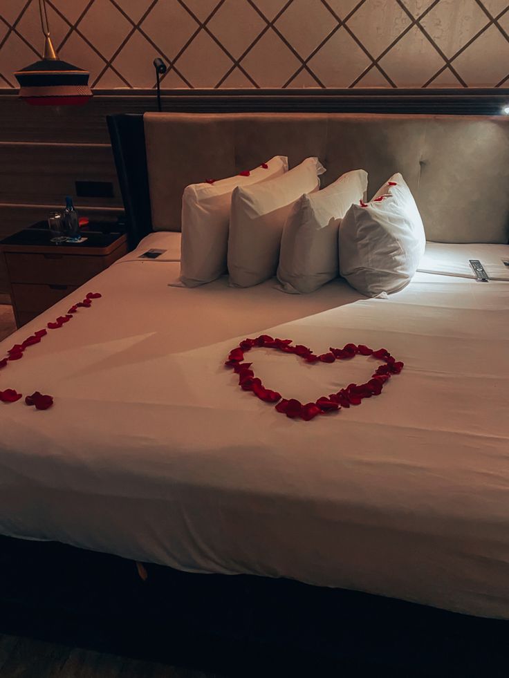 a bed with red rose petals on it and a heart shaped pillow in the middle