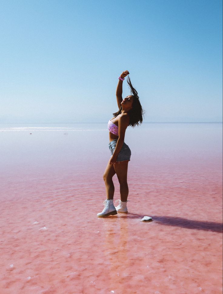 a woman standing in the middle of a pink lake with her arms up and legs crossed