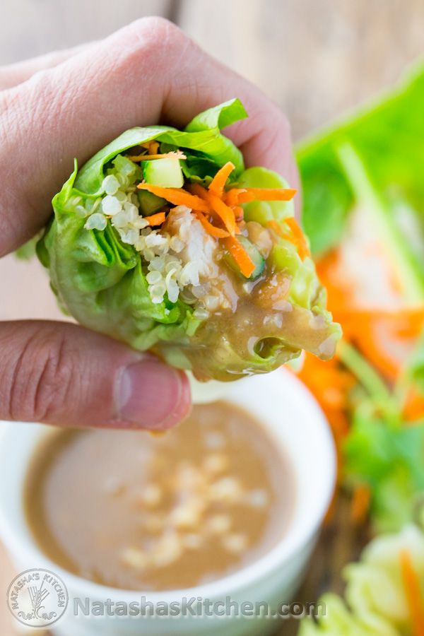 a person holding up a vegetable wrap with dipping sauce on the side and lettuce